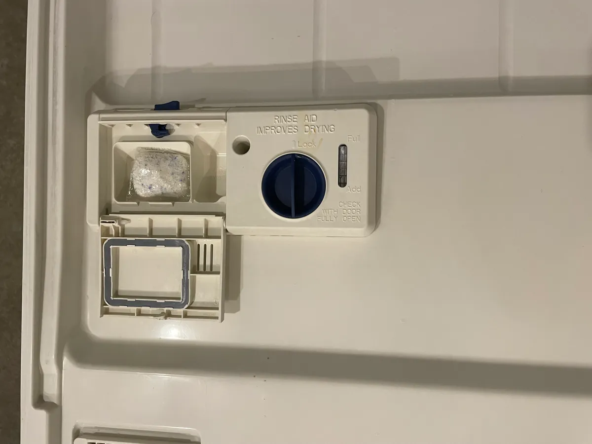 A dishwasher detergent tablet being placed in the door dispenser