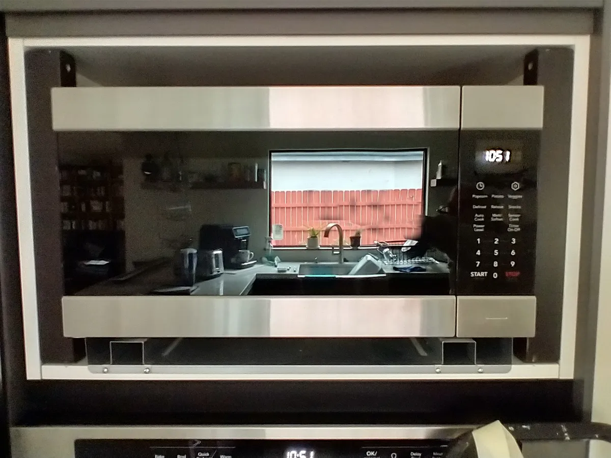 A microwave being installed into a kitchen cabinet unit