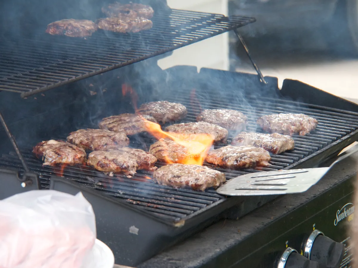Hamburger patties cooking on a hot propane grill grate