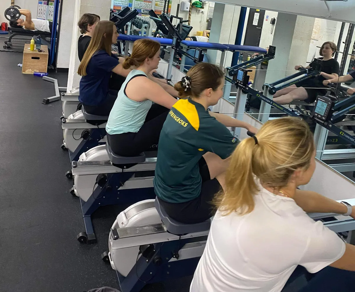 A row of ergometer rowing machines lined up in a college gym