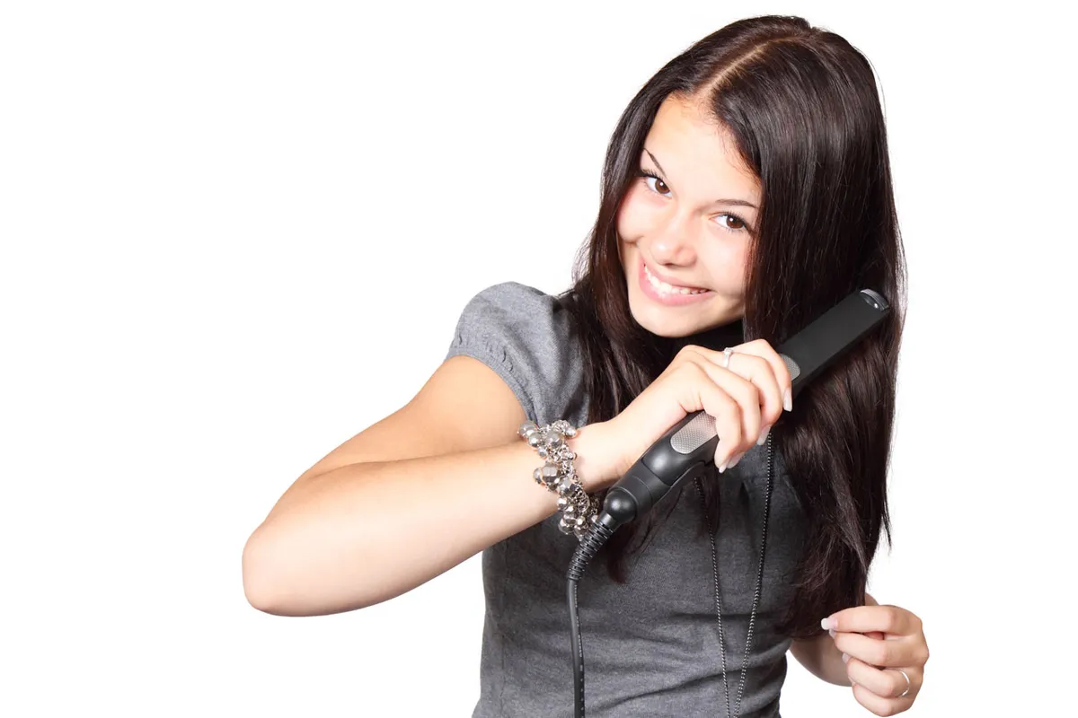 A person using a handheld hair styling tool to work through a section of hair, illustrating typical at-home styling posture
