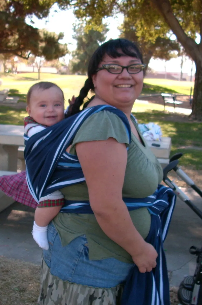 Stretchy fabric wrap-style baby carrier laid flat, illustrating the lower-cost alternative to a structured buckle carrier