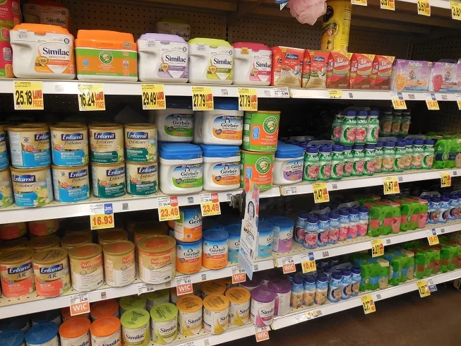 Shelf of infant formula canisters at a grocery store, representing the variety of formula brands a mixing machine must calibrate for