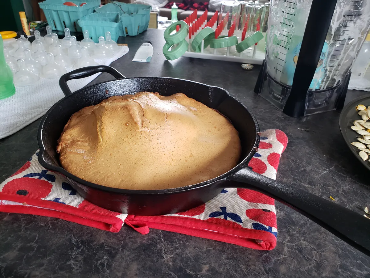 Puffed dutch baby pancake in a cast iron pan resting on oven mitts