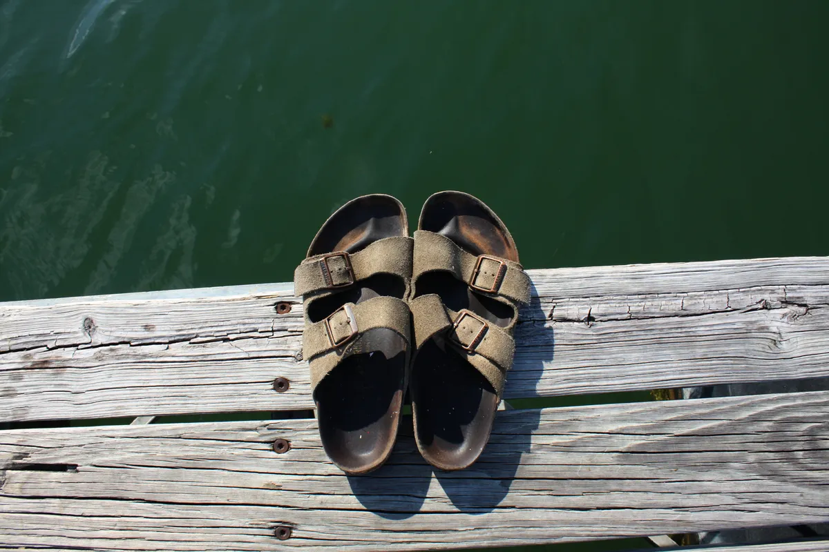 Birkenstock sandals left beside water on a stony shore