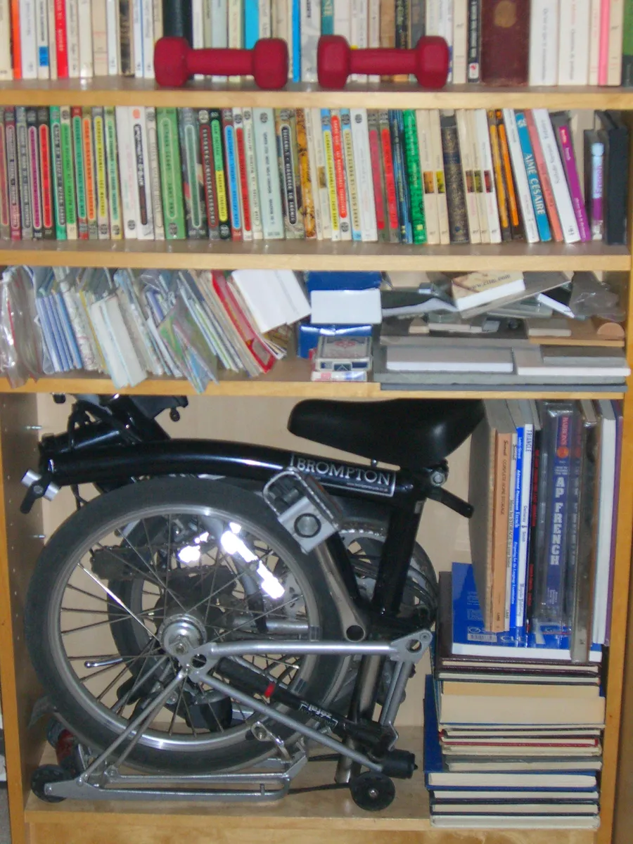 Fully folded Brompton bicycle stored inside a bookcase