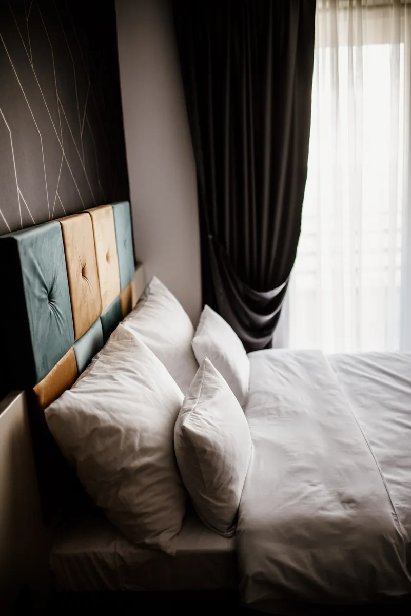 A bedroom with a made bed, layered pillows and curtains